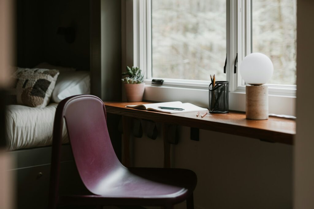 A chair and desk by a window with a lamp.